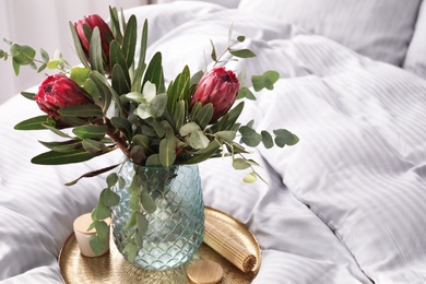 Photo of Vase with bouquet of beautiful Protea flowers on bed indoors