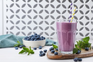 Photo of Glass of blueberry smoothie with mint and fresh berries on white wooden table, space for text