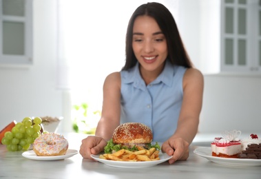 Photo of Concept of choice. Woman taking plate with tasty burger and French fries in kitchen, focus on food