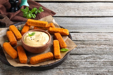 Delicious chicken nuggets and cheese sauce with basil on wooden table, space for text