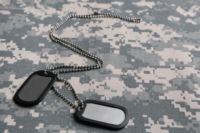 Metal military ID tags on camouflage background. Space for text