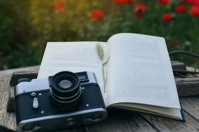 Open book with spike and vintage camera on wooden table outdoors, closeup