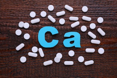 Paper symbol Ca (Calcium) and pills on wooden table, top view