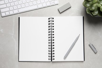 Open blank notebook, keyboard and stationery on light grey marble table, flat lay