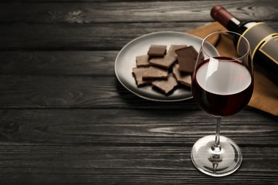 Tasty red wine and chocolate on black wooden table. Space for text