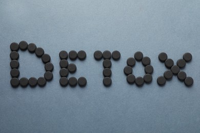 Word Detox made of activated charcoal pills on grey background, flat lay. Potent sorbent