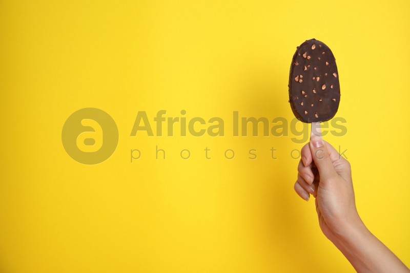 Photo of Woman holding ice cream glazed in chocolate on yellow background, closeup. Space for text