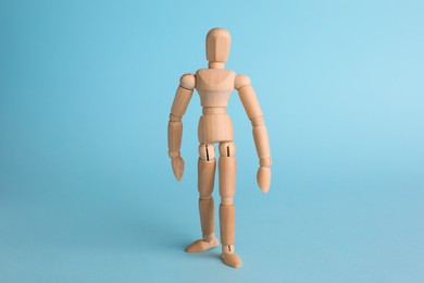 Wooden human model on light blue background. Mini mannequin