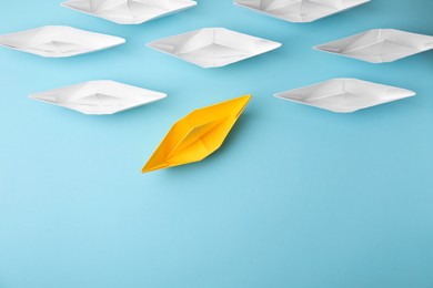 Photo of Yellow paper boat floating away from others on light blue background, flat lay with space for text. Uniqueness concept