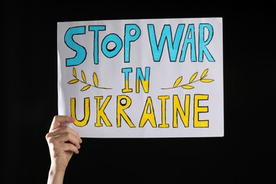 Teenage boy holding poster Stop War in Ukraine against black background, closeup