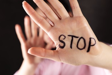 Woman with word Stop written on hand against dark background, closeup. Domestic violence concept