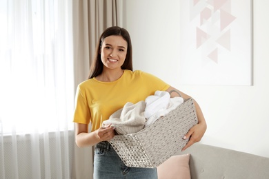 Young woman with laundry basket full of clean towels indoors