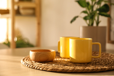 Yellow cups and wooden bowl on wicker mat in kitchen