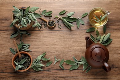 Flat lay composition with cup of sage tea, green leaves and teapot on wooden table. Space for text