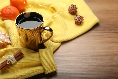 Photo of Cup of hot drink with yellow sweater and Christmas lights on wooden table. Space for text