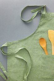 Photo of Clean apron with wooden kitchen tools on light grey background, top view