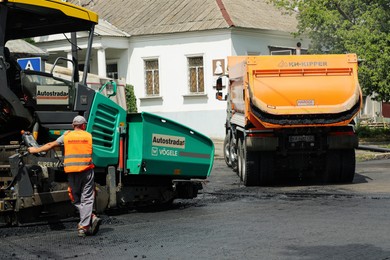 MYKOLAIV, UKRAINE - AUGUST 04, 2021: Worker with road repair machinery laying new asphalt