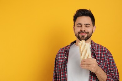 Photo of Young man eating tasty shawarma on yellow background. Space for text