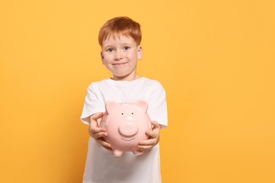Photo of Cute little boy holding ceramic piggy bank on orange background