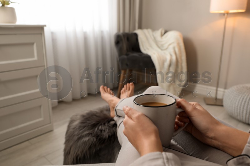 Woman with cup of hot drink resting at home, closeup. Space for text