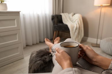 Woman with cup of hot drink resting at home, closeup. Space for text