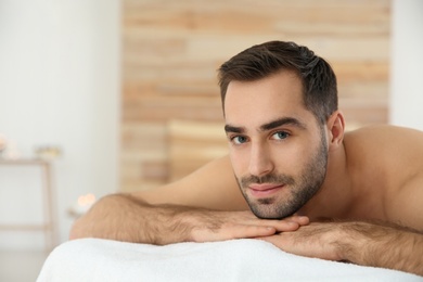 Photo of Handsome man relaxing on massage table in spa salon. Space for text