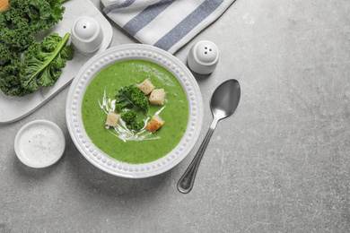 Tasty kale soup with croutons served on grey table, flat lay