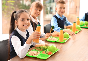 Happy children at table with healthy food in school canteen