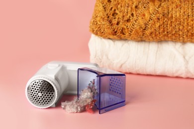 Photo of Modern fabric shaver with fuzz and knitted clothes on pink background, space for text