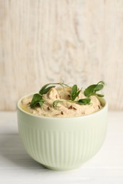 Photo of Bowl of tasty hummus with pea leaves on white wooden table, space for text