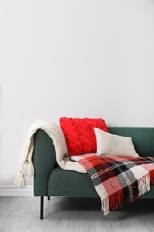 Sofa with soft pillows and warm plaids near light wall indoors. Space for text