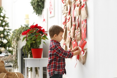 Photo of Cute little boy taking gift from Advent calendar at home. Christmas tradition