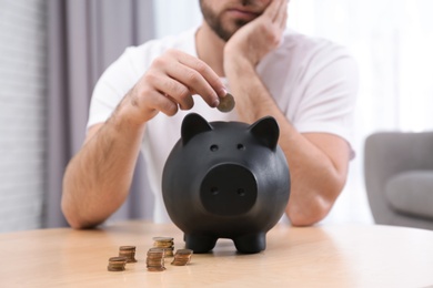 Sad young man with piggy bank saving money at home, closeup