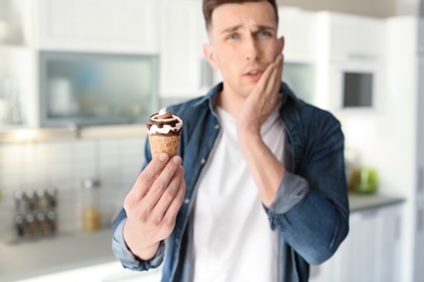 Young man with sensitive teeth and cold ice cream in kitchen