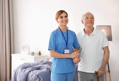 Nurse in uniform assisting elderly woman indoors. Space for text