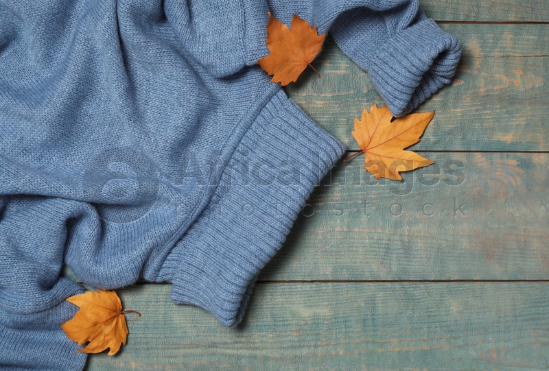 Photo of Warm sweater and dry leaves on blue wooden background, flat lay. Autumn season