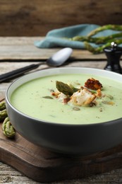 Bowl of delicious asparagus soup on wooden table, closeup