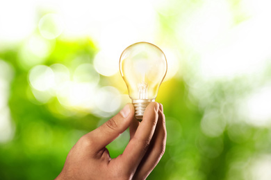 Solar energy concept. Man holding glowing light bulb against green blurred background, closeup