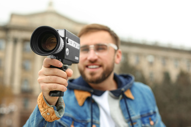 Young man with vintage video camera on city street, focus on lens