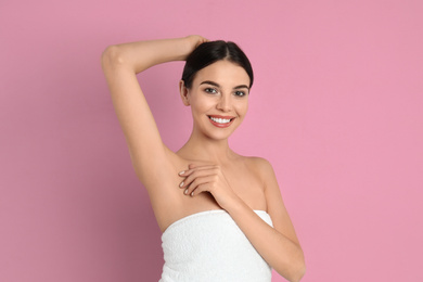 Young woman showing hairless armpit after epilation procedure on pink background