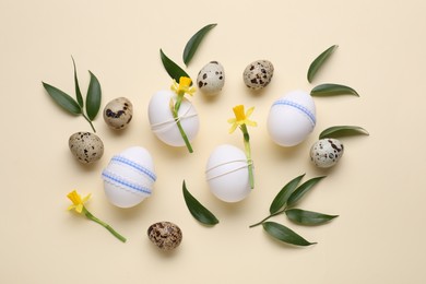 Photo of Festively decorated Easter eggs, green leaves and flowers on beige background, flat lay