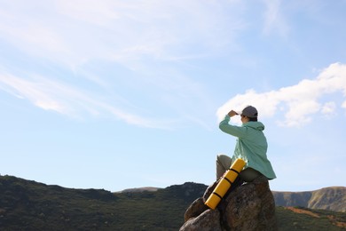 Young woman with backpack on rocky peak in mountains. Space for text
