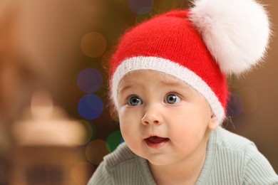 Cute little baby and blurred Christmas lights on background, space for text. Winter holiday