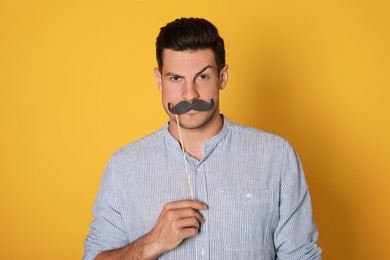 Photo of Funny man with fake mustache on yellow background