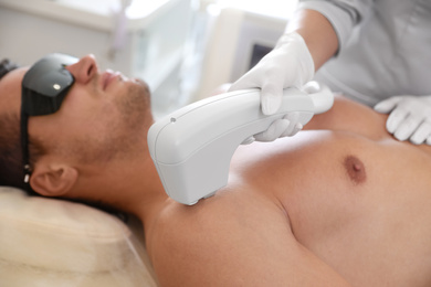 Young man undergoing laser epilation procedure in beauty salon, closeup