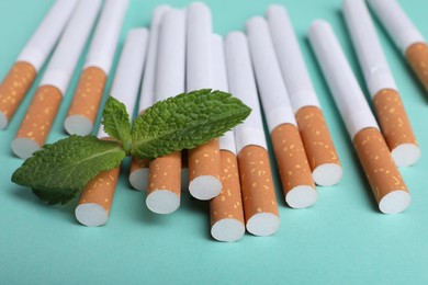 Menthol cigarettes and mint on turquoise background, closeup