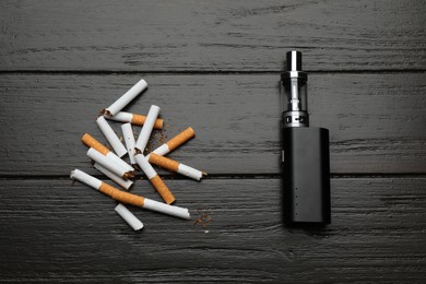 Broken cigarettes and vaping device on black wooden background, flat lay. Smoking alternative