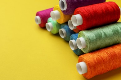 Different colorful sewing threads on yellow background, closeup. Space for text