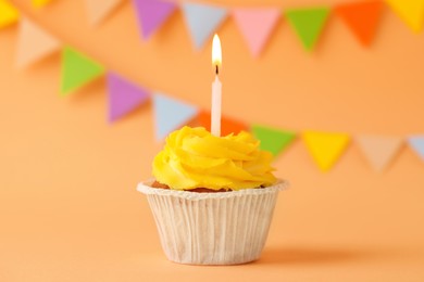 Tasty birthday cupcake with candle on orange table against party flags
