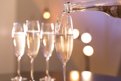 Champagne pouring from bottle into glass on blurred background, closeup. Space for text